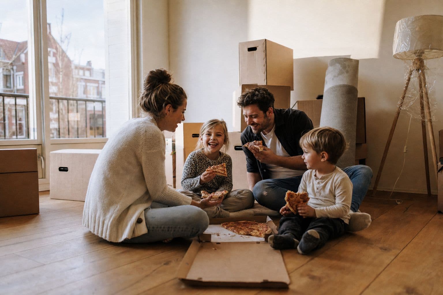 Gezin eet pizza op de vloer van hun nieuwe woning tussen de verhuisdozen